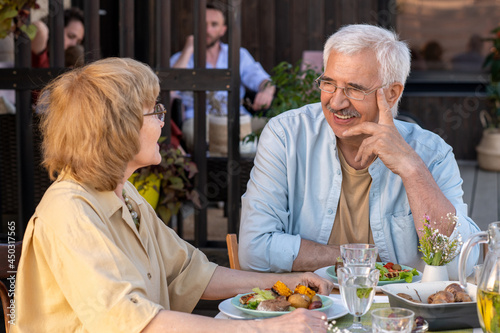 Cheerful senior man and his wife discussing something by family dinner outdoors