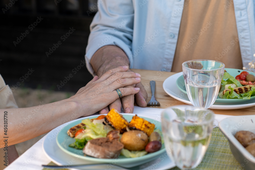 Hands of mature affectionate couple sitting by served table and having dinner