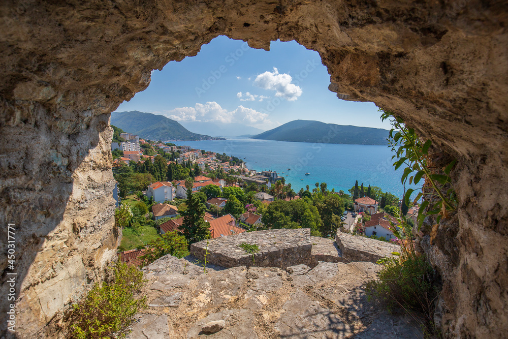 View of the city of Herceg Novi, blue sea and buildings through the hole in the stone wall of the fortress, Montenegro