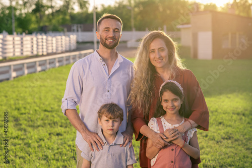 Happy young contemporary family of father, mother, daughter and son standing on green lawn