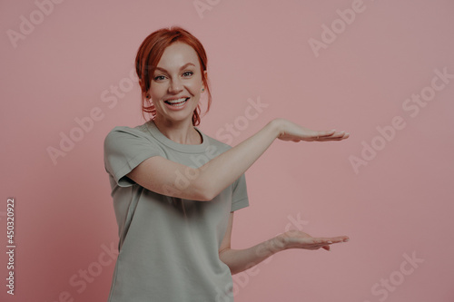 Young pleasant red-haired woman showing huge product size or something big with hands photo