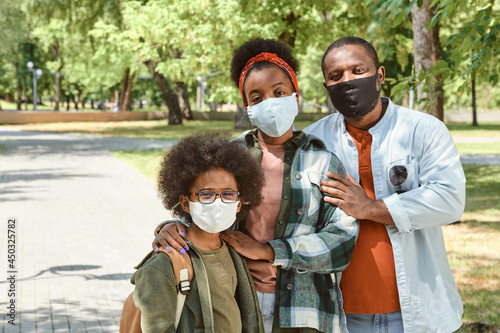 Young affectionate African family in masks standing in park on summer day