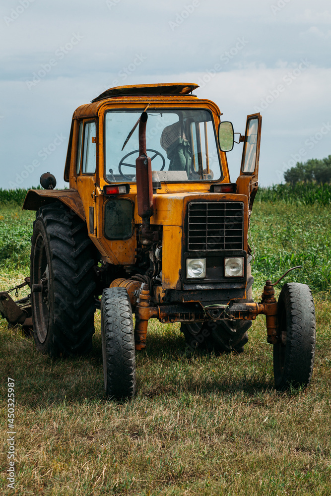 an old rusty yellow tractor stands in a green field not a background of corn in the afternoon an old rusty yellow tractor stands in a green field not a background of corn in the afternoon