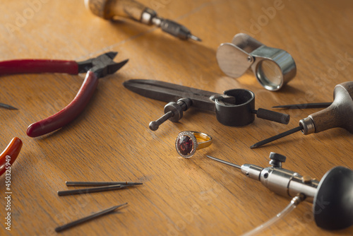 Luxury golden ring with ruby gemstone on jeweler's workbench. Workplace of a jeweler. Tools and equipment for jewelry work on an antique wooden desktop.
