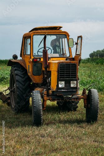 an old rusty yellow tractor stands in a green field not a background of corn in the afternoon