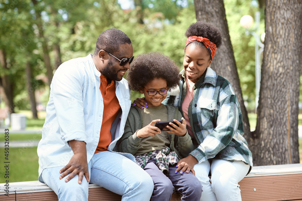 Happy family with smartphone communicating through video chat while resting in park Happy family with smartphone communicating through video chat while resting in park