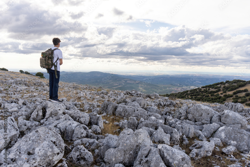 Teenager boy standing on a rock looking towards the horizon in a rocky field Teenager boy standing on a rock looking towards the horizon in a rocky field