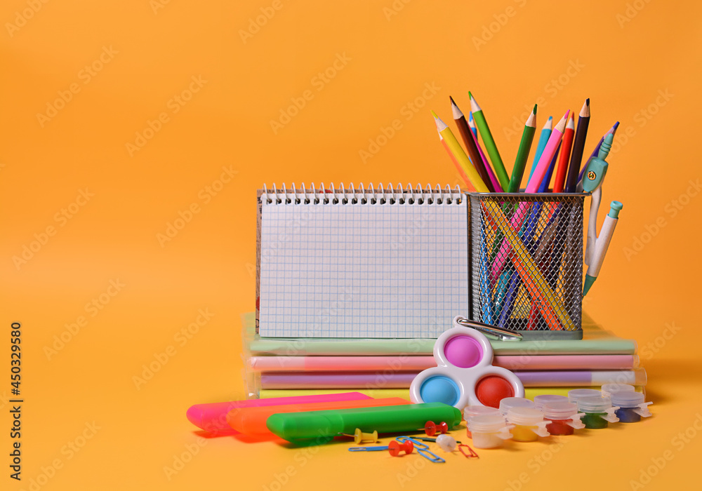 School supplies: notebooks, books, colored pencils, simple dimple - New popular colorful silicone sensory trendy toy antistress on an orange background. Back to school. Copy space. - obrazy, fototapety, plakaty 