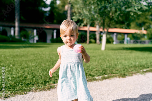 Little girl with a ball in her hand walks along the gravel path in the park