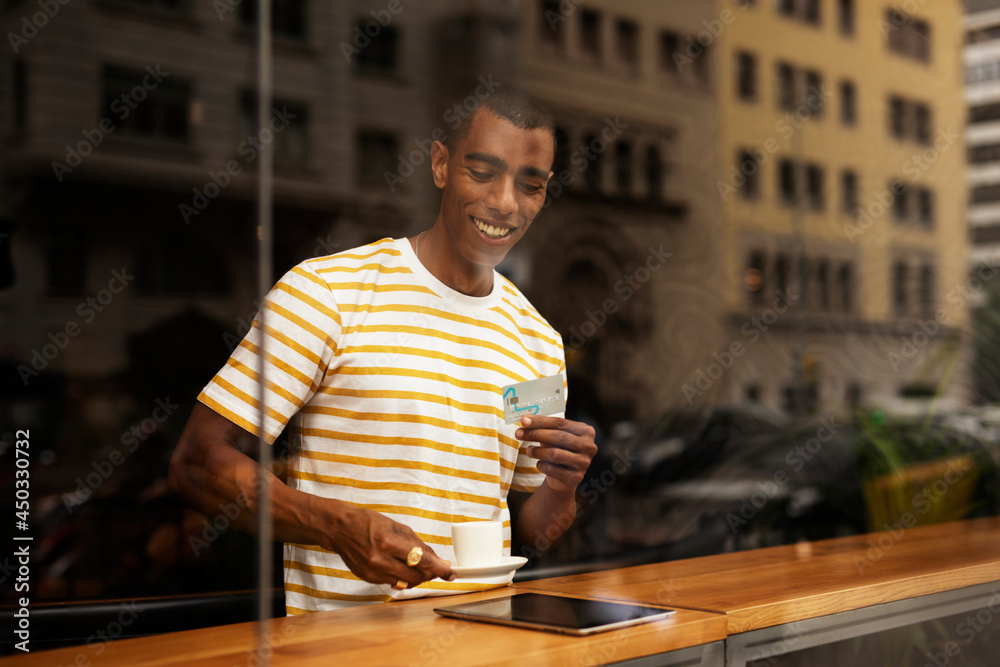 Handsome young african man in cafe drinking coffee. Portrait of happy man with credit card drinking coffee in cafe..