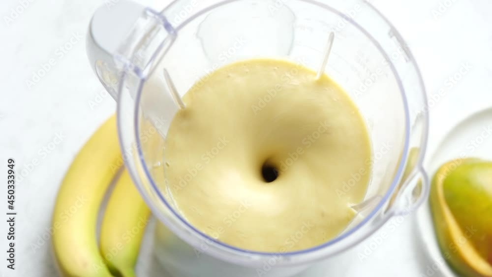 Tropical fruit Mango Banana smoothie preparing in blender. Process of mixing fruits in electric blender Tropical fruit Mango Banana smoothie preparing in blender. Process of mixing fruits in electric blender