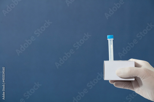 nurse's hands with surgical gloves, medium transport tube for pcr analysis, in cardboard holder, blue background