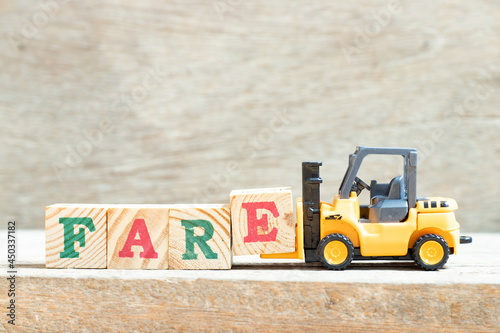 Toy forklift hold letter block e to complete word fare on wood background