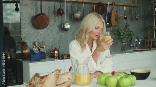 Beautiful mature woman in bathrobes having breakfast in the domestic kitchen