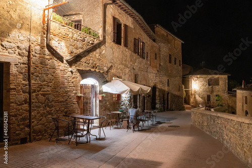 San Gimignano, Tuscany, Italy. August 2020. Picturesque night view on one of the streets of the historic center with the tables of a restaurant. From behind a customer is alone at a table. New normal.