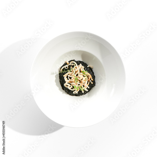 Risotto with cuttlefish black ink. Black risotto plate isolated on white background. Risotto with squid ink topped with calamari rings. Gourmet restaurant dish over white background.