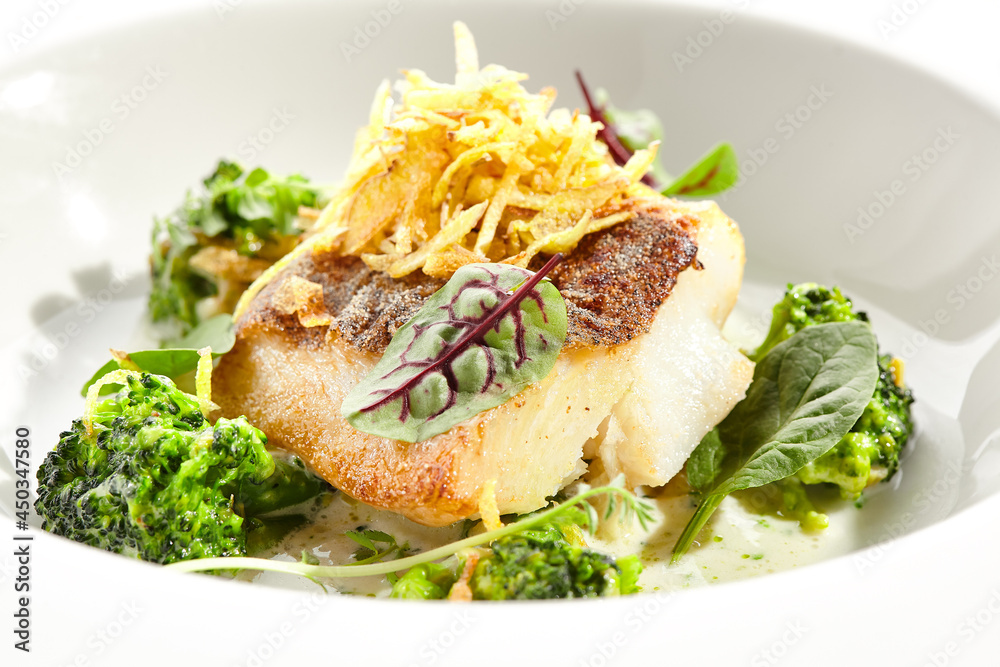Panfried Fish with broccoli and cream sauce. Healthy roasted cod with green leaves. Fried Fish on white restaurant plate isolated on white background.