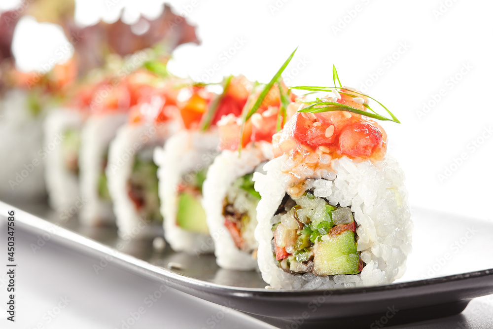 Healthy vegetarian Japanese lunch. Vegan sushi roll with avocado and mushrooms inside. Topped with tomato. Vegetarian sushi rolls dish. Restaurant asian vegan food isolated on white background. Healthy vegetarian Japanese lunch. Vegan sushi roll with avocado and mushrooms inside. Topped with tomato. Vegetarian sushi rolls dish. Restaurant asian vegan food isolated on white background.