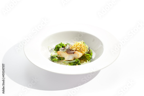 Panfried Fish with broccoli and cream sauce. Healthy roasted cod with green leaves. Fried Fish on white restaurant plate isolated on white background.