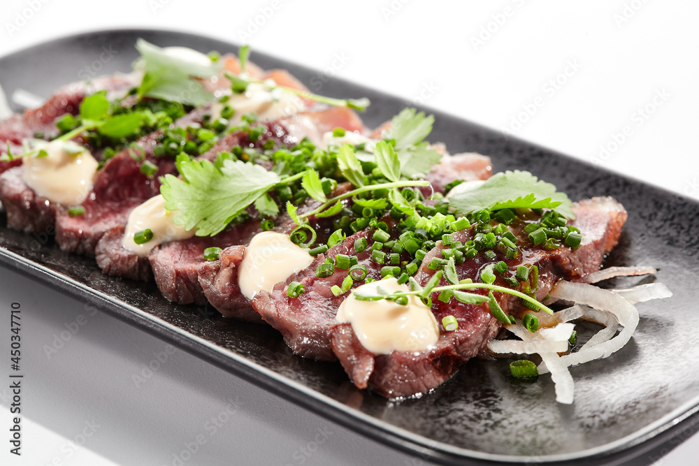 Beef tataki - seared beef,. thinly sliced sashimi style. Beef tataki served with delicious ponzu tataki sauce. Japanese style meat on black plate isolated on white background.. Beef tataki - seared beef,. thinly sliced sashimi style. Beef tataki served with delicious ponzu tataki sauce. Japanese style meat on black plate isolated on white background..