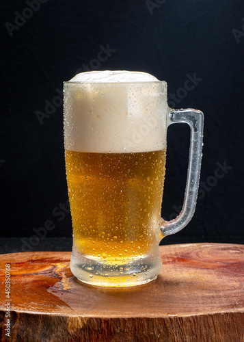 Beer mug, served cold with plenty of foam on a wooden board on a black background