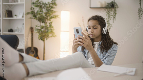 African teen girl with headset watching videos on smartphone, gadget addiction