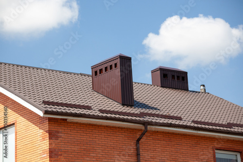 Red metal roof tile and smokestack. Modern chimney on brown roof.