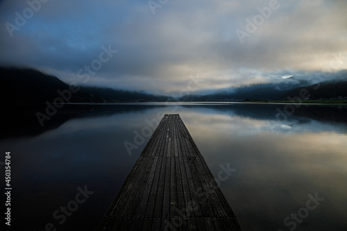 Fototapeta Naklejka Na Ścianę i Meble -  立ち込む雲が映りこんだ静かな朝の湖に伸びる一本の木製桟橋