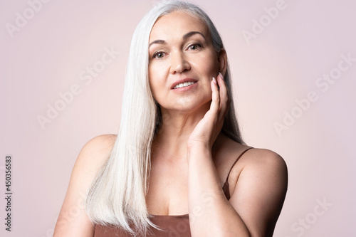 Elderly gray-haired female looking at camera. Positive single mature senior retired woman touching healthy groomed perfect face skin. Natural old beauty and aging concept. photo