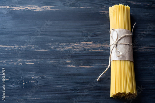 Raw spaggetti wrapped in brown craft paper tied with twine on a dark wooden background. Copy space photo