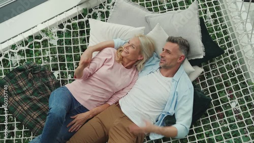 Top view of mature couple communicating while relaxing in hammock at home 