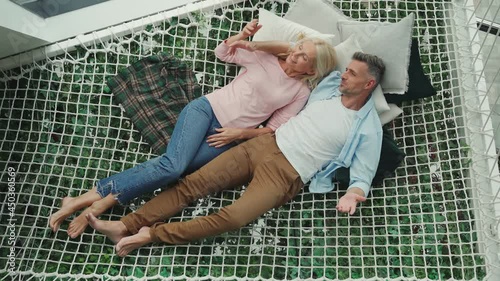 Top view of mature couple communicating while relaxing in hammock at home 