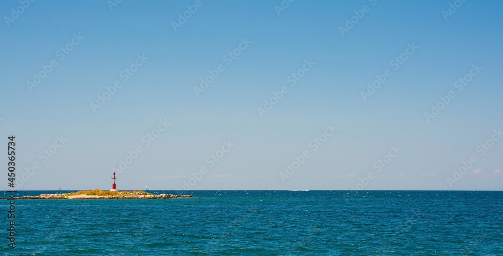 A small unmanned lighthouse in Adriatic Sea seen from the coastal path around the historic medieval town of Porec in Istria, Croatia
