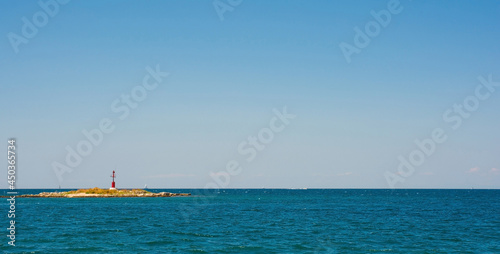 A small unmanned lighthouse in Adriatic Sea seen from the coastal path around the historic medieval town of Porec in Istria, Croatia
