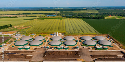 Green biogas plant storage tanks. Aerial view over biogas plant and farm in green fields. Renewable energy from biomass. Modern agriculture concept