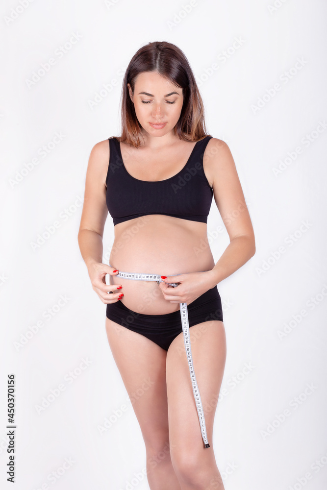 Obraz premium Young pregnant woman measuring her belly and smiling. The anticipation of motherhood
