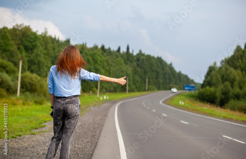 The girl stops the car on the highway with her hand. Stylish woman on the road stops the car go on a journey. A road in the middle of the forest.