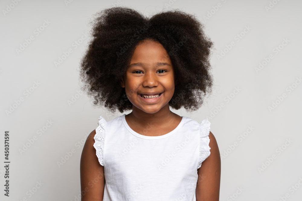 Portrait of happy preschool curly girl in T-shirt joyfully looking at camera and smiling, proud of own success. Indoor studio shot isolated on white background