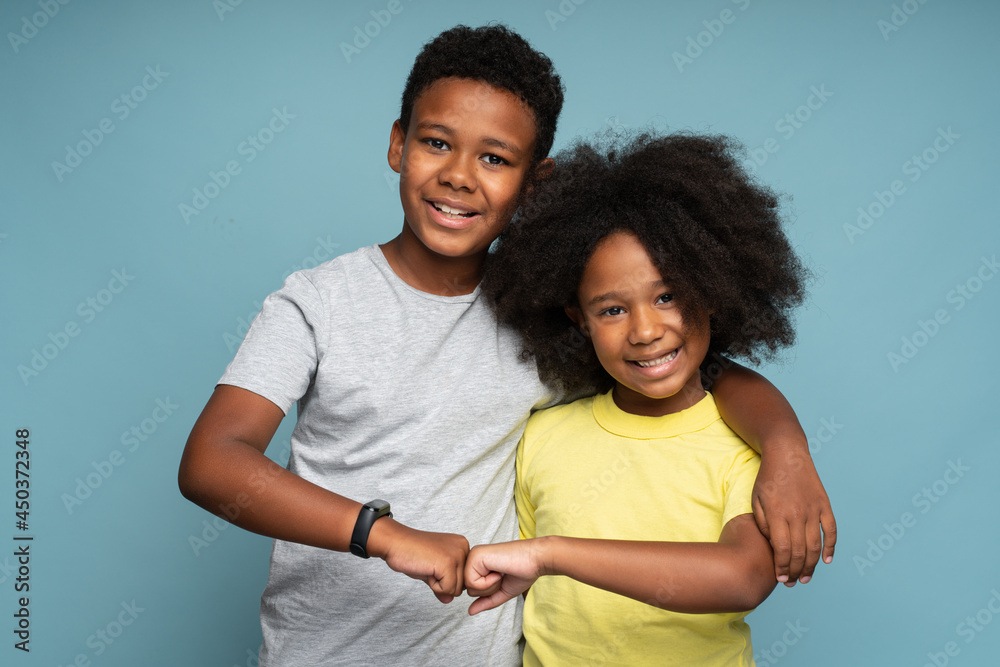Awesome. Portrait of positive couple of brother and sister in casual style standing, hugging and bumping with fists with toothy smile, while looking at camera. Isolated, indoor, studio shot Awesome. Portrait of positive couple of brother and sister in casual style standing, hugging and bumping with fists with toothy smile, while looking at camera. Isolated, indoor, studio shot