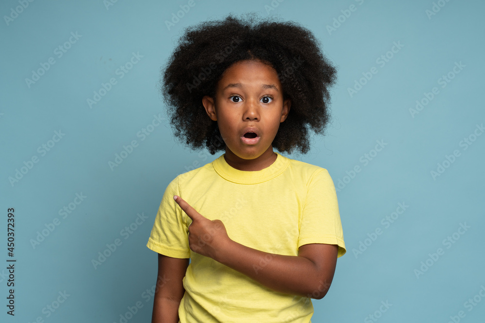 Wow awesome. Amazed excited cute little girl pointing at something and looking at camera with shocked face. Child feeling surprised. Indoor studio shot blue background