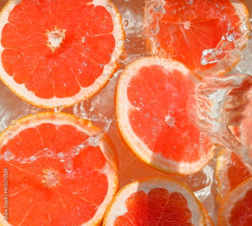Slices of grapefruit in water on white background. Grapefruit close-up in liquid with bubbles. Slices of blood red ripe grapefruit in water. Macro image of fruits in water