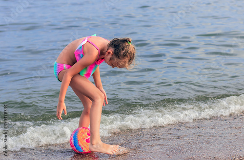 girl 6-7 years old, blonde, in a bright swimsuit, plays with a inflatable ballon the seashore, portrait of a child in a bikini in full growth, on the beach