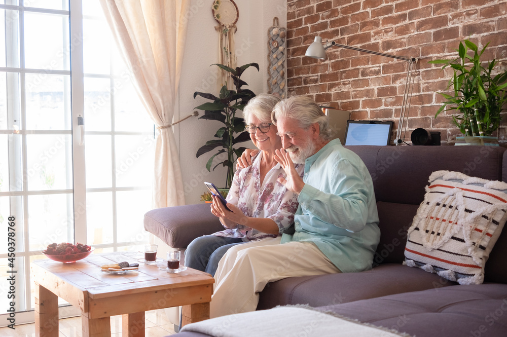Obraz premium Two smiling senior people in video call with mobile phone. Sitting at home on sofa