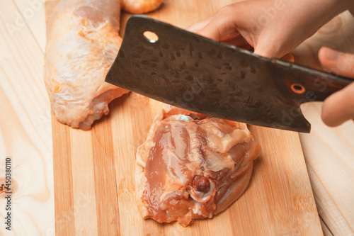Female hands cut a chicken thigh at the junction of the bones with a chef's cleaver