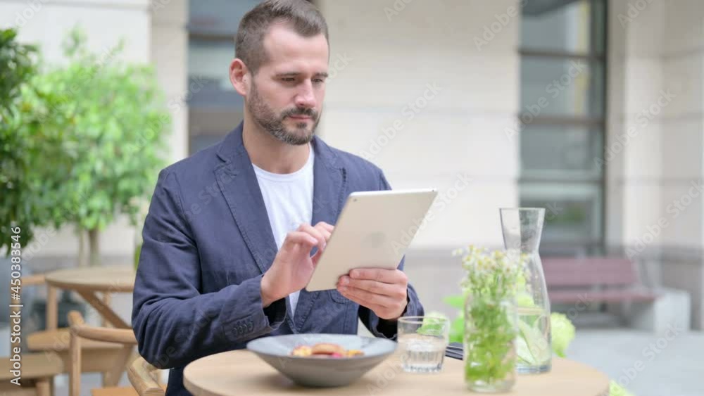 Man Browsing Internet on Tablet while Sitting in Outdoor Cafe Man Browsing Internet on Tablet while Sitting in Outdoor Cafe