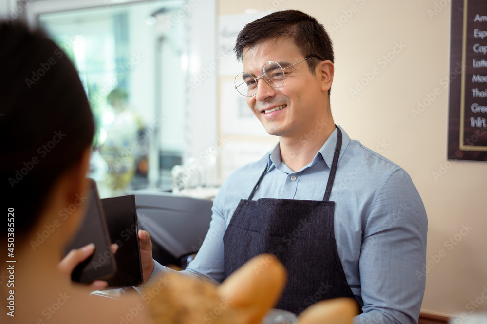 Obraz premium Smiling barista giving online payment to customer , pay for the order in a cafe shop