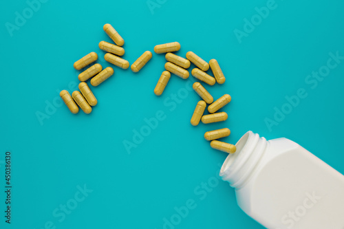 yellow dietary supplement capsules poured out of the white unbranded jar on turquoise background. medical bottle mockup. medical template for branding, text and design