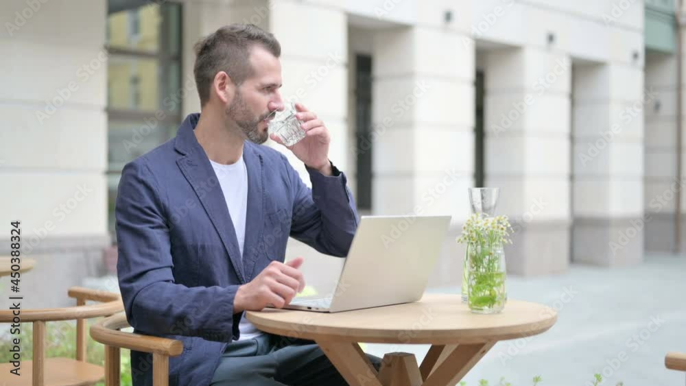 Man Drinking Water while Working on Laptop, Sitting in Outdoor Cafe Man Drinking Water while Working on Laptop, Sitting in Outdoor Cafe