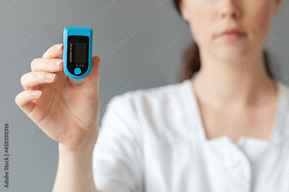 Blurred portrait of doctor shows a pulse oximeter. Gray background. The concept of health care and check health