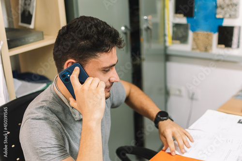 Young man with dark hair, working in an office, and talking on the phone